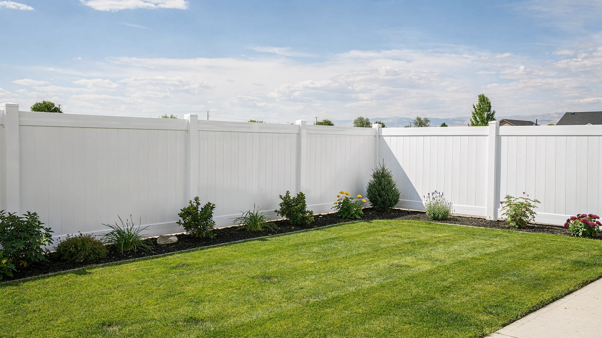 A clean white vinyl privacy fence surrounding a neat Twin Falls backyard with a lawn, small garden beds, and open Idaho sky in the background.