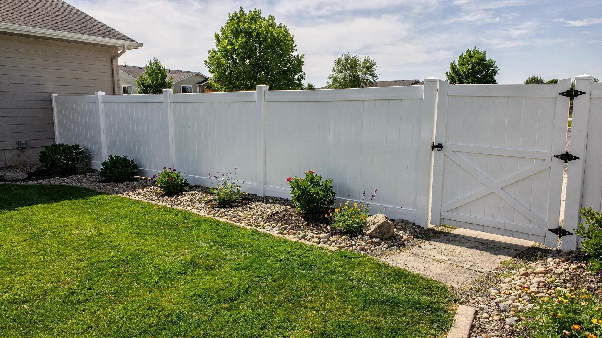 A well-built vinyl privacy fence surrounding an Idaho backyard with lawn, landscaping, and a gate leading to a side yard.